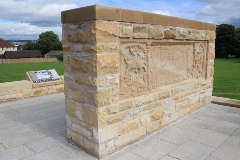 Roman replica in sandstone surrounded by stone wall.